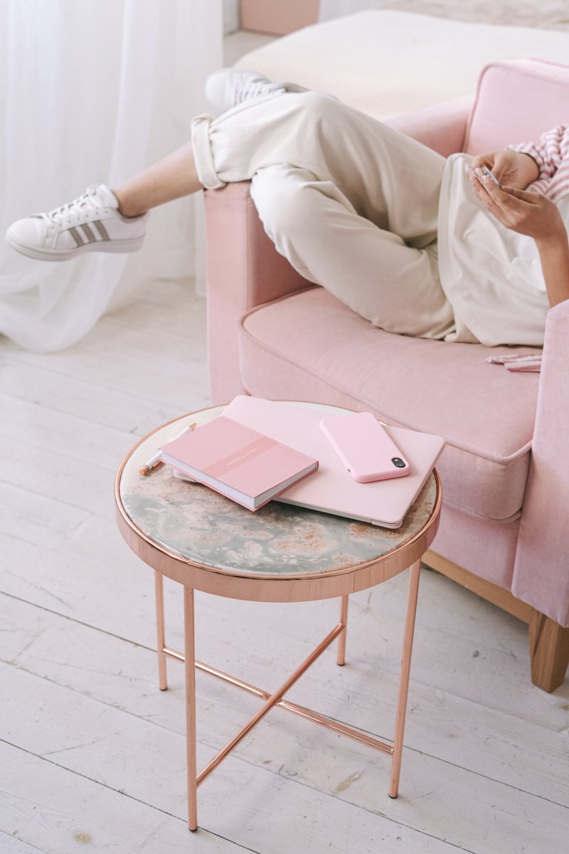 A Person Sitting on Pink Chair Near a Table with Notebook and Cellphone